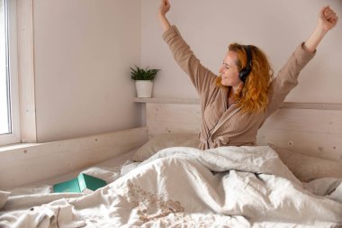 Neşeli, güzel, kızıl saçlı kız evde kaldı, sevindi, güldü ve sevdiği şeyi yaptı. Yatakta kulaklıkla müzik dinledi..