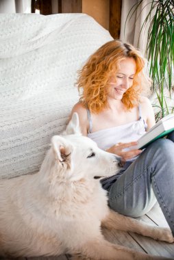 Genç, gülümseyen bir kız sevgili evcil hayvanıyla iletişim kuruyor. İsviçreli beyaz bir çoban köpeği. Kitap okuyor..