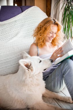 Genç, gülümseyen bir kız sevgili evcil hayvanıyla iletişim kuruyor. İsviçreli beyaz bir çoban köpeği. Kitap okuyor..
