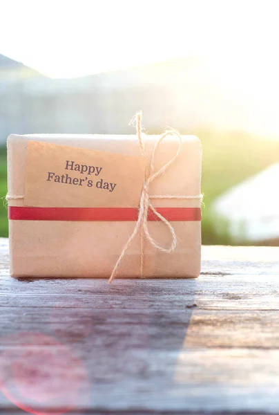 Geschenkdoos op een houten tafel in de stralen van de ondergaande zon. Selectieve focus. Gefeliciteerd met Vaderdag.. — Stockfoto