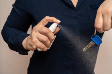 Kadın dezenfekte etmek ve virüsleri öldürmek için kapı anahtarına alkol el dezenfektanı sıkıyor.