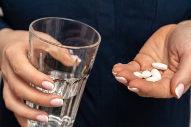 Bir avuç beyaz antivirüs hapı ve büyük bardak su tutan bir kadın.