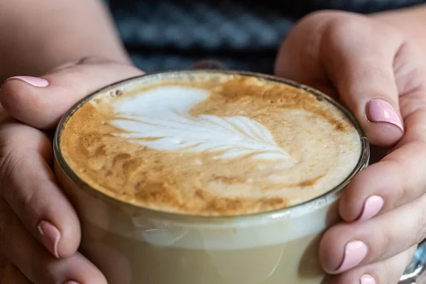 Closeup of woman hands hug a very big mug of cappucino with coffee art