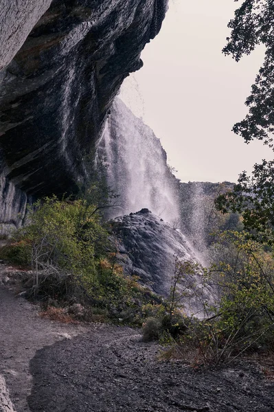 views of a waterfall with water falling on a large rock in the foreground