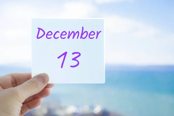 December 13th. Hand holding sticker with text December 13 on the blurred background of the sea and sky. Copy space for text. Month in calendar concept — Stock Photo, Image