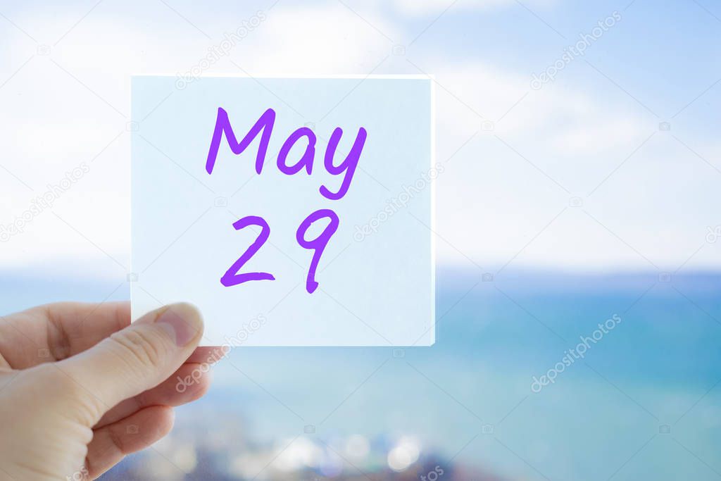 May 29th. Hand holding sticker with text May 29 on the blurred background of the sea and sky. Copy space for text. Month in calendar concept