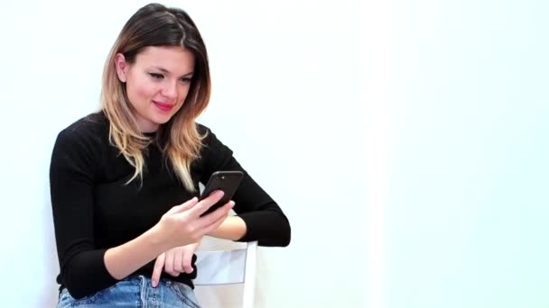 Atraktivní žena na bílém pozadí se dívá na svůj telefon a vzrušený mnoha záliby v sociální síti — Stock video