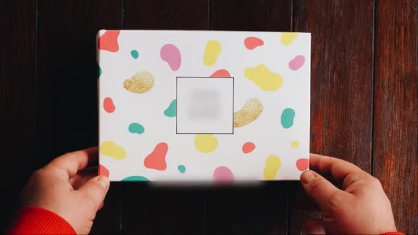 Mannelijke handen open een kleurrijke doos met vier verschillende eetlust eclairs op houten achtergrond — Stockvideo