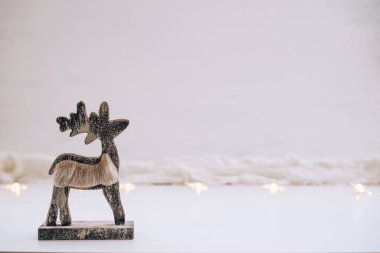 Kar ve ışıklardan oluşan beyaz bir zemin üzerinde ahşap geyik heykeli olan Noel arkaplanı