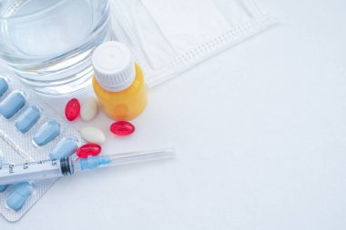 Tıbbi muayene ve tedavi konsepti. Kırmızı ve beyaz haplar, termometre, sarı serum, maske, mavi arka planda tıbbi şırınga fotokopi alanı. Tıbbi düzlük