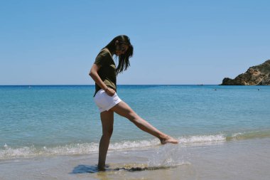 Beyaz şortlu, siyah tişörtlü, beyaz bir kadın yazın plajda dikiliyor.