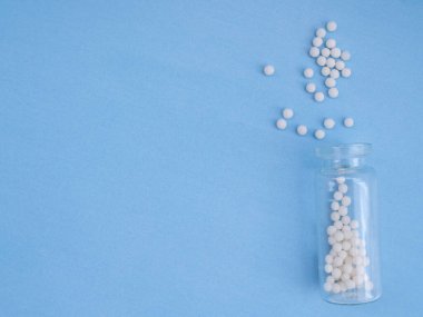 Mavi arka planda homeopatik globullar ve cam şişe. Homeopatik Tıp