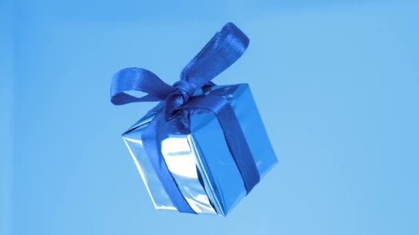 Подарочная коробка с голубой лентой, вращающейся на синем фоне. 360 градусов вращения — стоковое видео