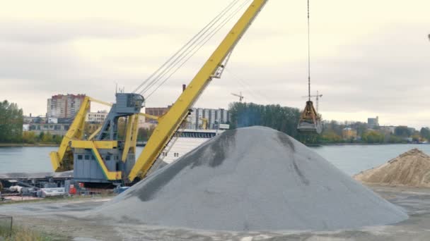 Ekskavator kuning menuangkan tumpukan puing di depan sungai. Embernya tergantung di kabel . — Stok Video