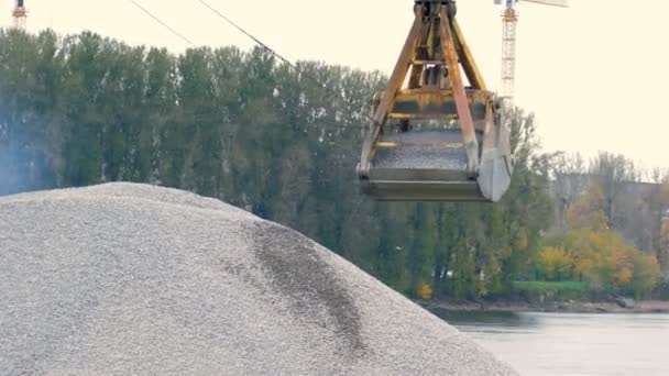 Excavator bucket pours a mountain of rubble on the background of the river — Αρχείο Βίντεο