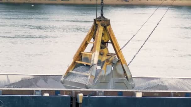 Ковші екскаватора викидають гравій із залізного контейнера на тлі річки — стокове відео