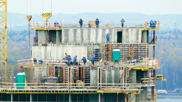 Trabajadores de la construcción montando encofrados de hormigón con grúa durante la construcción de viviendas en el fondo del bosque y la carretera — Vídeos de Stock