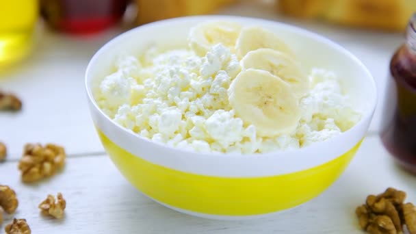 Healthy breakfast - crumbly, cottage cheese with banana, walnuts, croissants, honey and lingonberry jam in a bowl standing on a wooden table — Stock Video