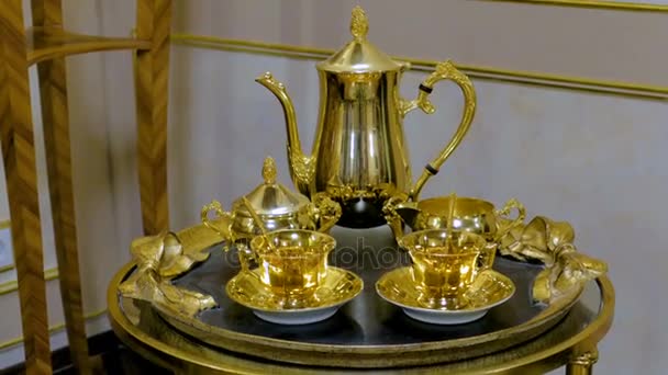 Tea set made of gold on the tray. It consists of two mugs, sugar bowls, teapot and spoons — Stock Video