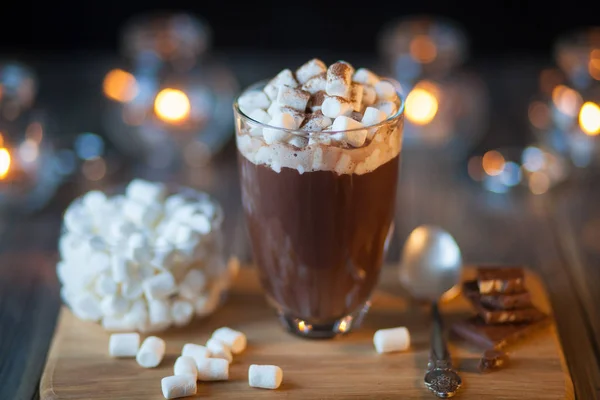 Beautiful composition - hot chocolate with marmalade and  pieces in a transparent glass. The  stands on  wooden stand. Behind the candles are burning — Stock Photo, Image