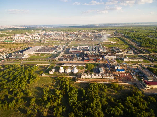 Una enorme refinería de petróleo con tuberías y destilación del complejo en un campo verde rodeado de bosque. Vista aérea —  Fotos de Stock