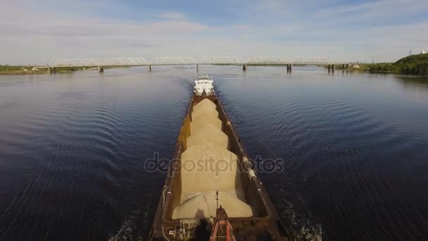 Pråm lastad med sand och grus flyter på den breda floden på bakgrunden av bron. Flygfoto — Stockvideo