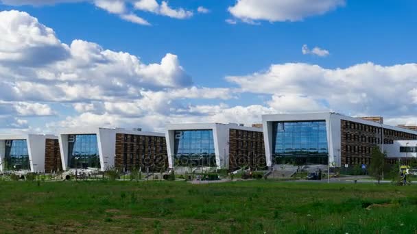 Bürogebäude auf der Wiese mit Glasfenstern, die die schwebenden Wolken reflektieren, entlang des Gebäudes stehen Menschen. Zeitraffer — Stockvideo