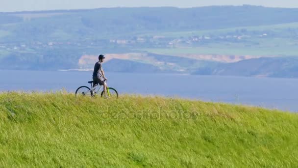 Ο ποδηλάτης κοιτάζει γύρω και κινείται κάτω από τον πράσινο λόφο — Αρχείο Βίντεο