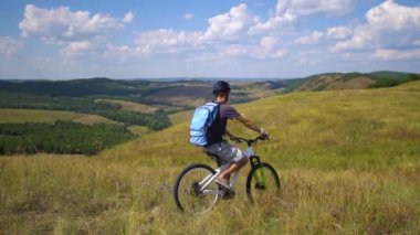 Bulutlu gökyüzü karşı yeşil bir tepeden aşağı genç adam bir bisiklet üzerinde rulo