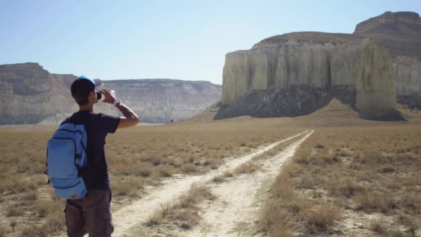 Een jonge reiziger drinkt water tegen de rotsen — Stockvideo