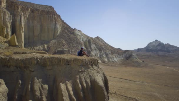 젊은 여행자는 절벽의 가장자리에 앉아서 물 음료 — 비디오