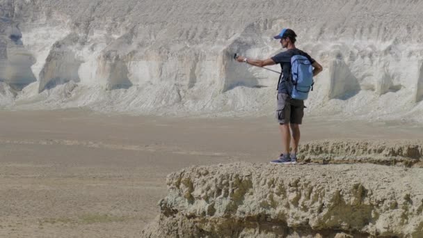 Ein junger Reisender steht am Rande einer Klippe und macht ein Selfie — Stockvideo