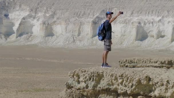 Ένας νεαρός ταξιδιώτης στέκεται στην άκρη ενός γκρεμού και κάνει μια selfie — Αρχείο Βίντεο