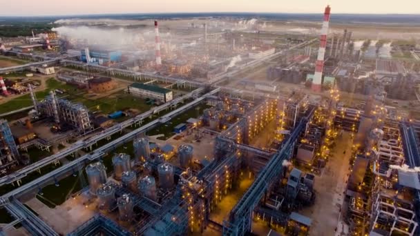 Ett stort oljeraffinaderi med metallkonstruktioner, rör och destillation av anläggningen med brinnande ljus i skymningen. Flygfoto — Stockvideo