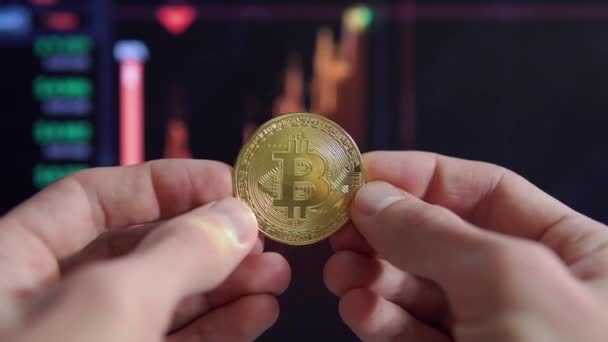 Mani maschili tengono una moneta d'oro bitcoin sullo sfondo di un tasso di cambio fluttuante — Video Stock