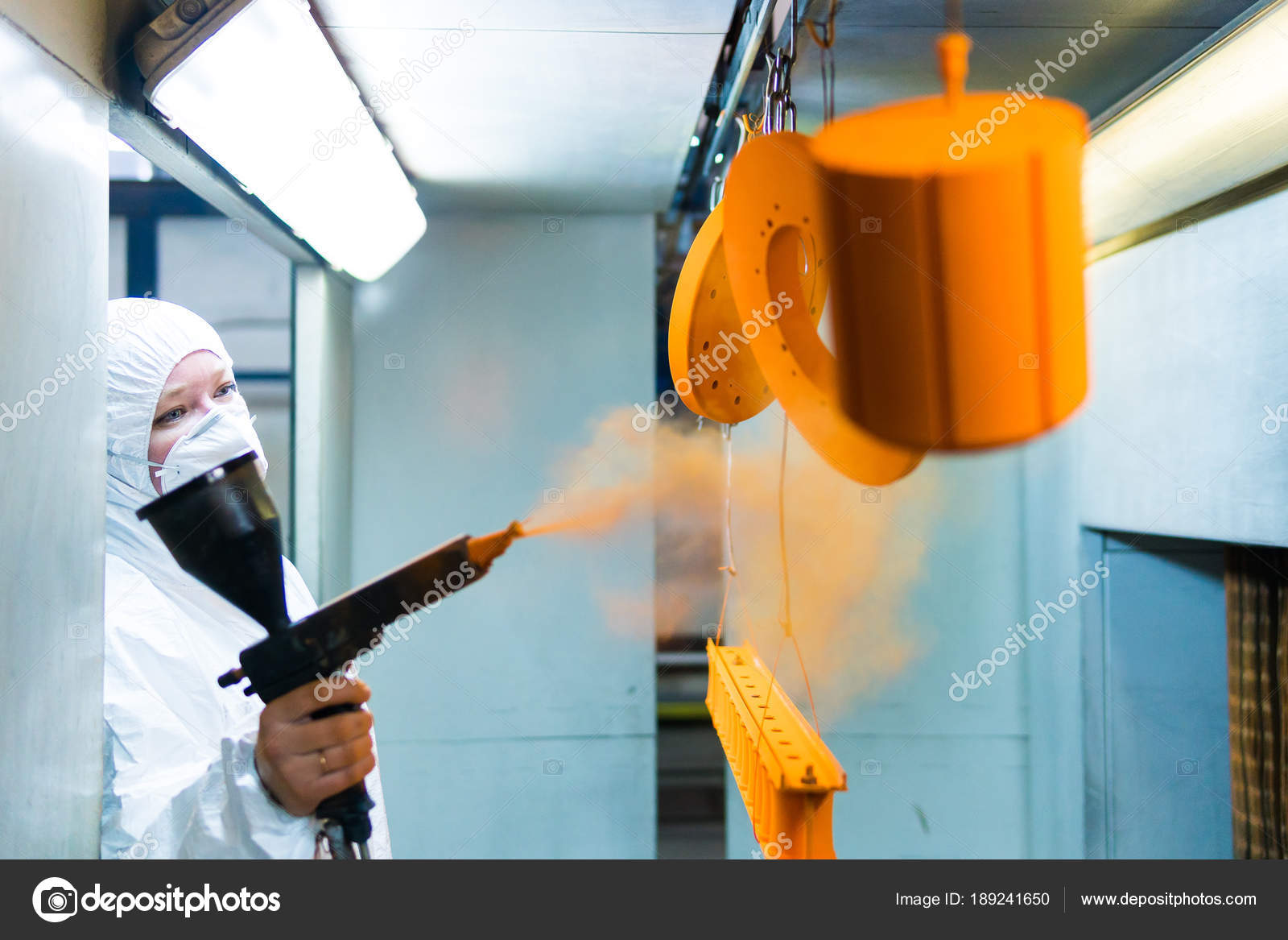 Powder coating of metal parts. A woman in a protective suit sprays ...