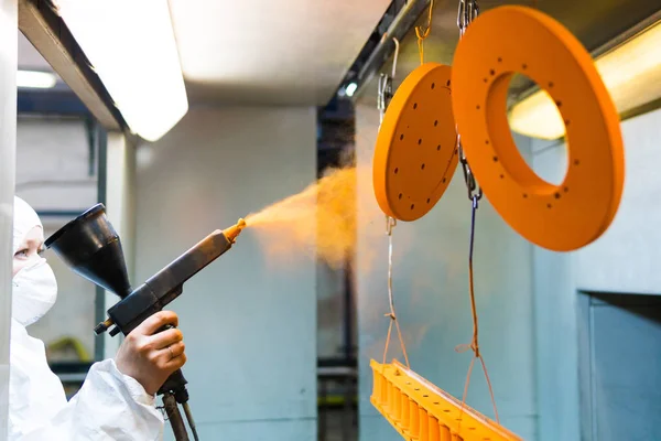 Recubrimiento en polvo de piezas metálicas. Una mujer con un traje protector rocía pintura en polvo de una pistola sobre productos metálicos — Foto de Stock