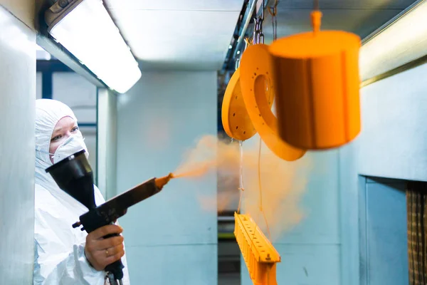 Revêtement en poudre de pièces métalliques. Une femme en combinaison de protection pulvérise de la peinture en poudre à partir d'un pistolet sur des produits métalliques — Photo