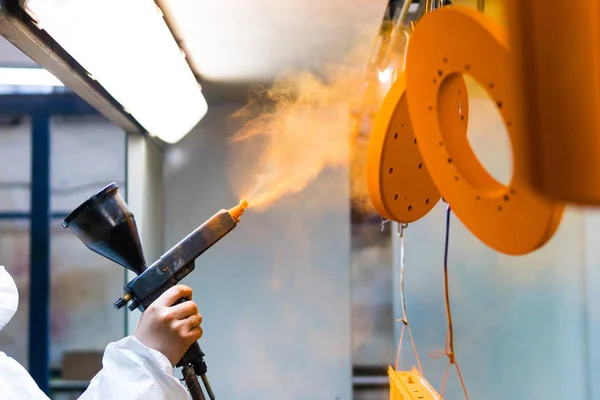 Pulverbeschichtung von Metallteilen. Eine Frau im Schutzanzug sprüht Pulverfarbe aus einer Pistole auf Metallprodukte — Stockfoto