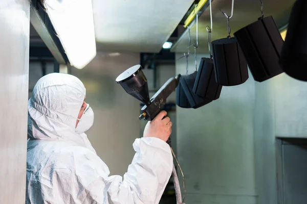 Revestimento em pó de peças metálicas. Um homem em um terno protetor pulveriza tinta em pó de uma arma em produtos metálicos — Fotografia de Stock