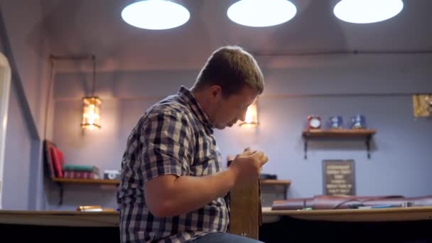 Muž v kostkované košili šije kousky kožené nitě. Vytváří kabelku pro individuální design v dílně — Stock video