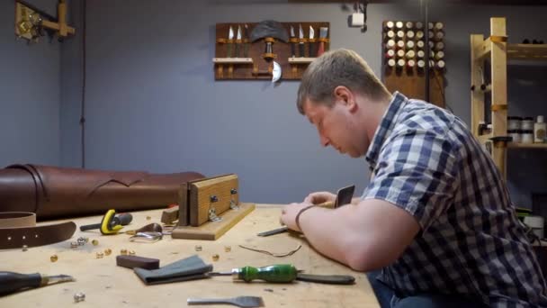 Tailor in a plaid shirt crea una bolsa de cuero para el diseño individual en el taller. — Vídeo de stock