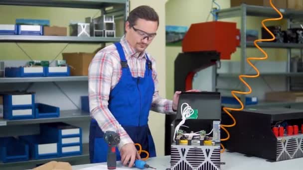 Jovem trabalhador de camisa e macacão monta componentes eletrônicos em uma fábrica de alta tecnologia — Vídeo de Stock