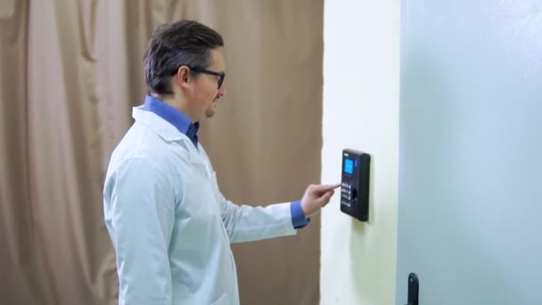 Йонг мужчина в лабораторном халате нажимает палец на сканер отпечатков пальцев, чтобы получить доступ к системам безопасности двери. Селективная направленность — стоковое видео