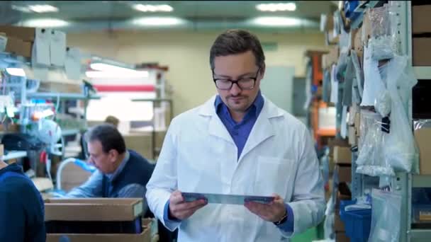 El ingeniero con una bata blanca y gafas inspecciona la placa madre lista. Procesamiento de PCB en la máquina CNC, producción de componentes electrónicos en la fábrica de alta tecnología — Vídeo de stock