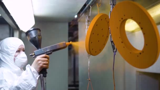 Revestimento em pó de peças metálicas. Uma mulher em um terno protetor pulveriza tinta em pó de uma arma em produtos metálicos — Vídeo de Stock