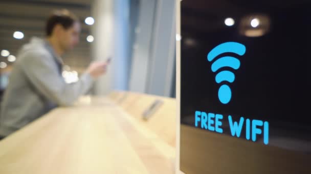 Mladý muž používá telefon na pozadí Free Wifi Signal bliká na displeji v kavárně — Stock video