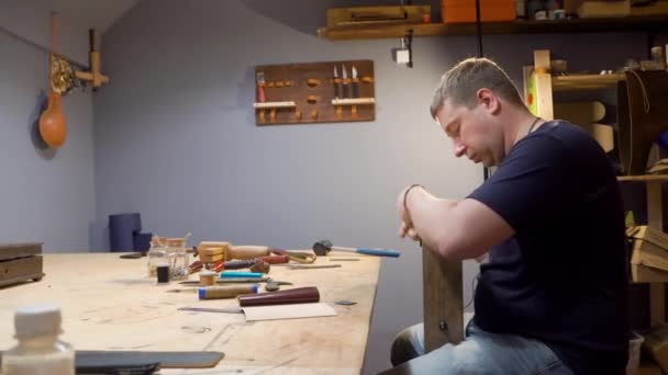 태너는 스튜디오에서 바늘 가죽 제품을 꿰매고 있다. 그는 개인 디자인을 위한 지갑을 만듭니다. — 비디오