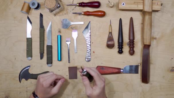 Primer plano de la pieza de corte maestro masculino de cuero con herramientas de elaboración para la cartera futura en el taller. Vista de ángulo alto del lugar de trabajo del zapatero — Vídeo de stock