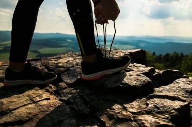 Koşucu ayakkabı bağını bağlarken ormanda spor yapmaya hazırlanıyor. Sabah güneşiyle birlikte kayanın üstünde.